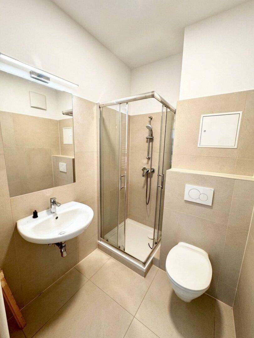 Modernes Badezimmer mit beigen Fliesen, Duschkabine und wandhängendem WC.