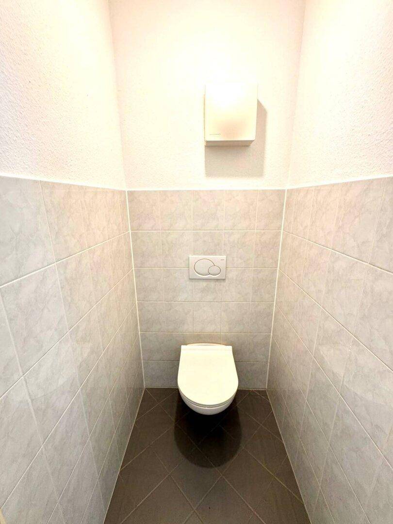 Kleines Gäste-WC mit wandhängender Toilette und hellen Fliesen an Wänden und Boden.