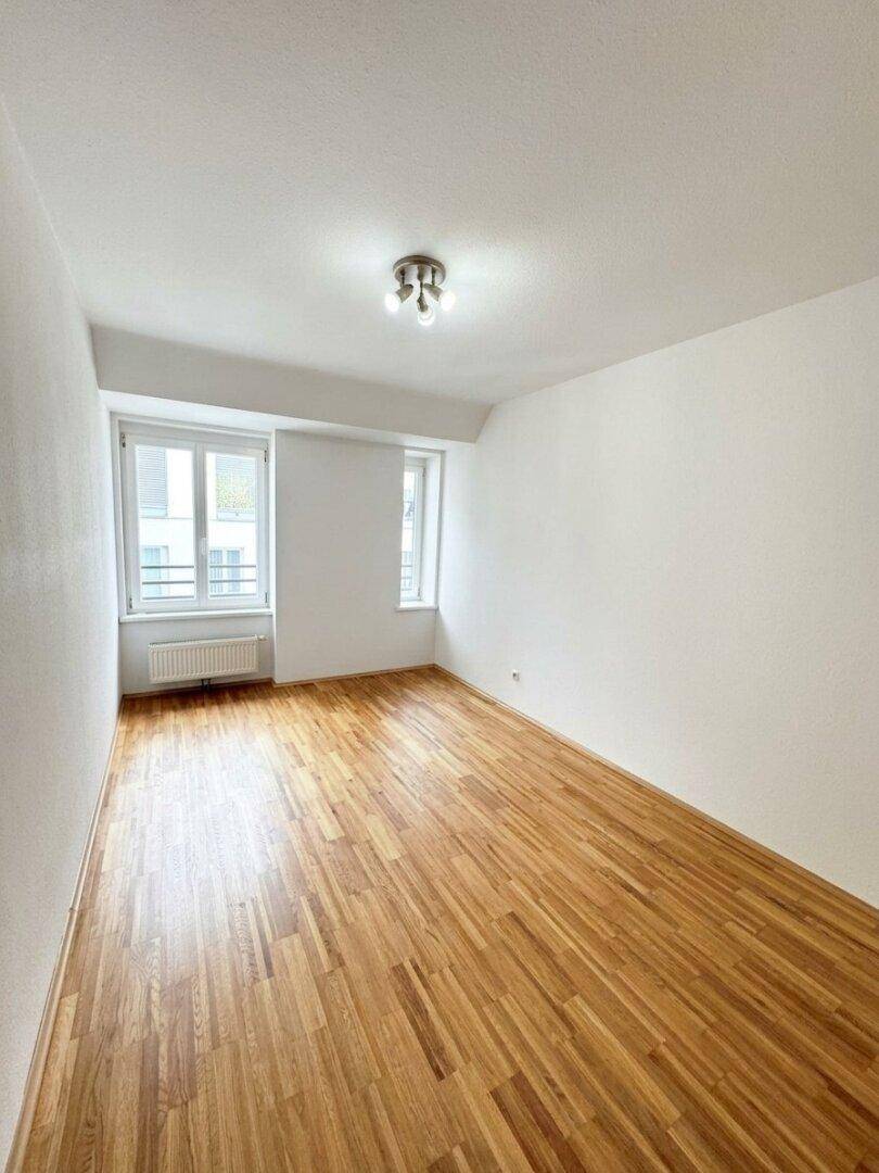 Geräumiges Schlafzimmer mit zwei Fenstern, Holzboden und viel natürlichem Licht.