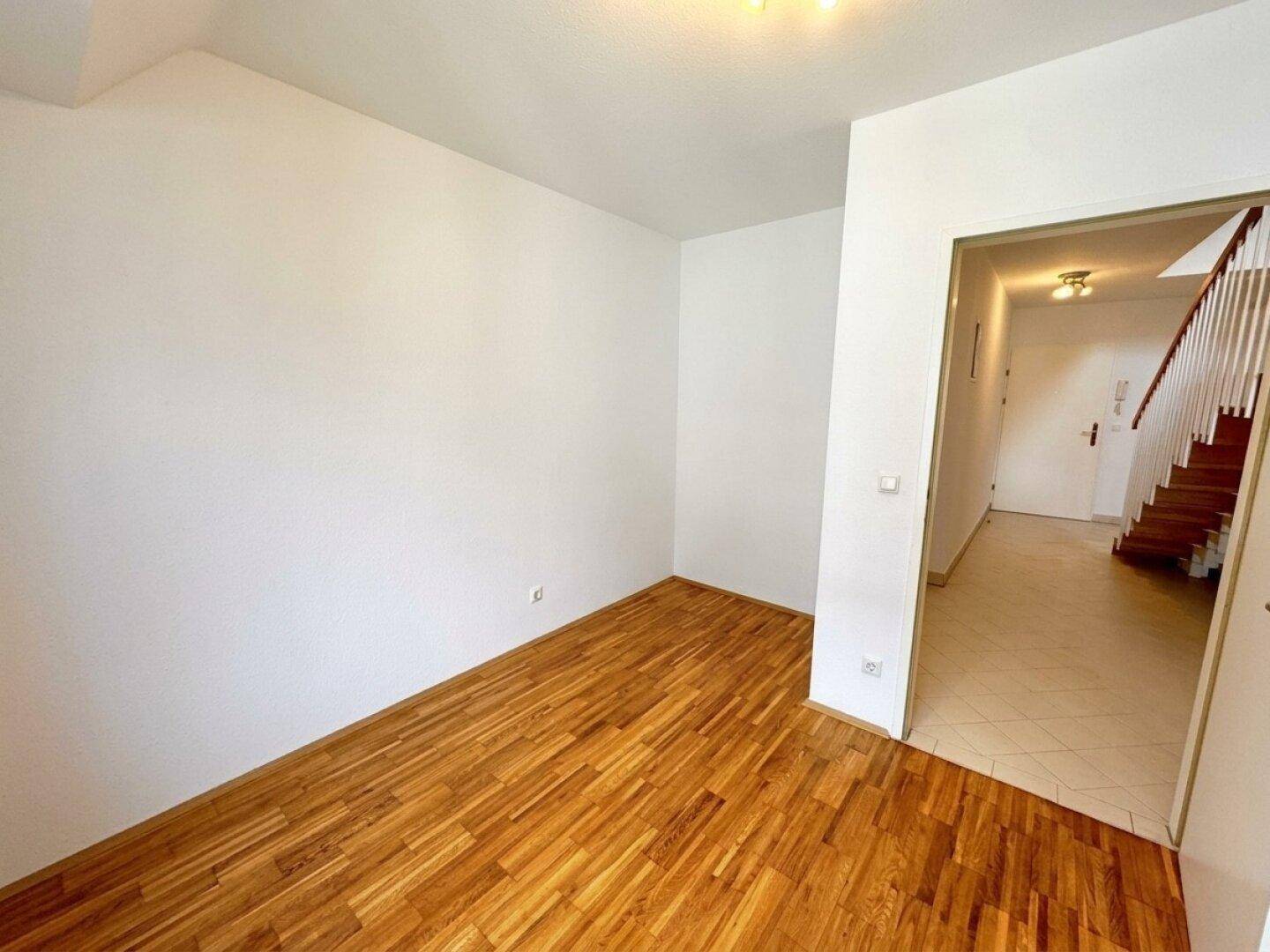 Heller Raum mit Holzboden und Zugang zu einem gefliesten Flur mit Treppe.