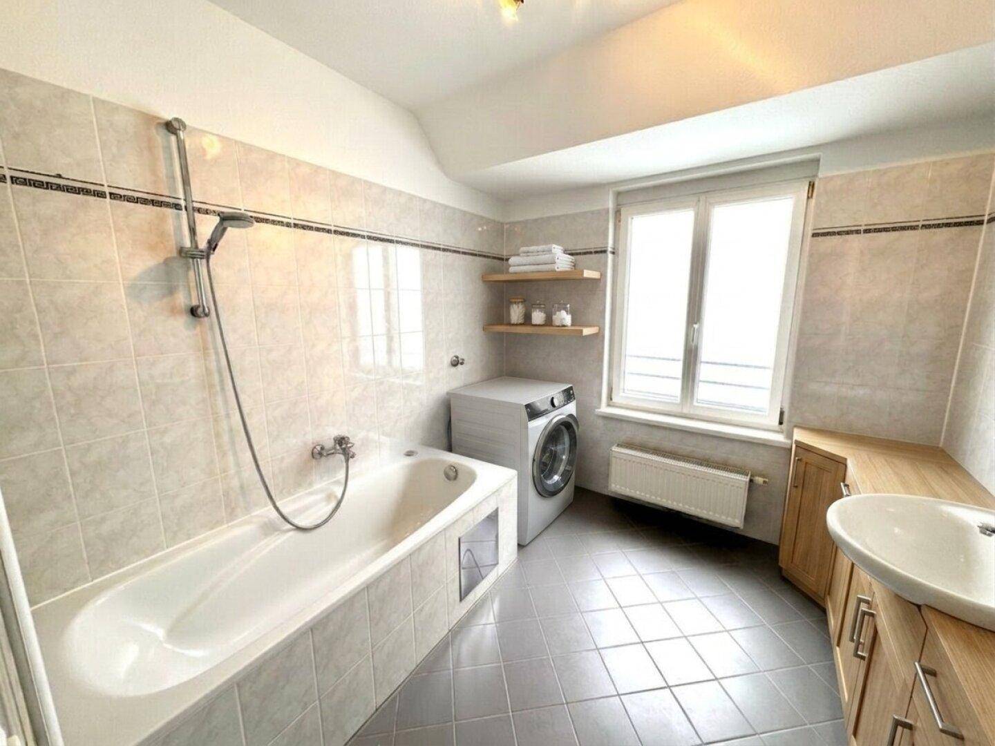 Badezimmer mit Badewanne, Waschmaschine, Holzwaschtisch und Fenster für Tageslicht.