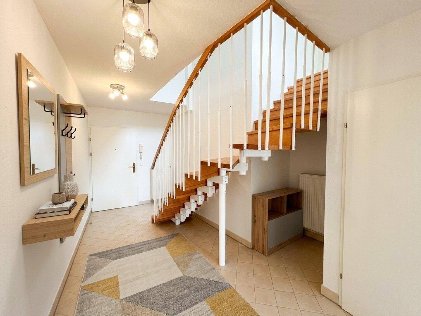 Heller Eingangsbereich mit Holztreppe, Fliesenboden und moderner Garderobe.