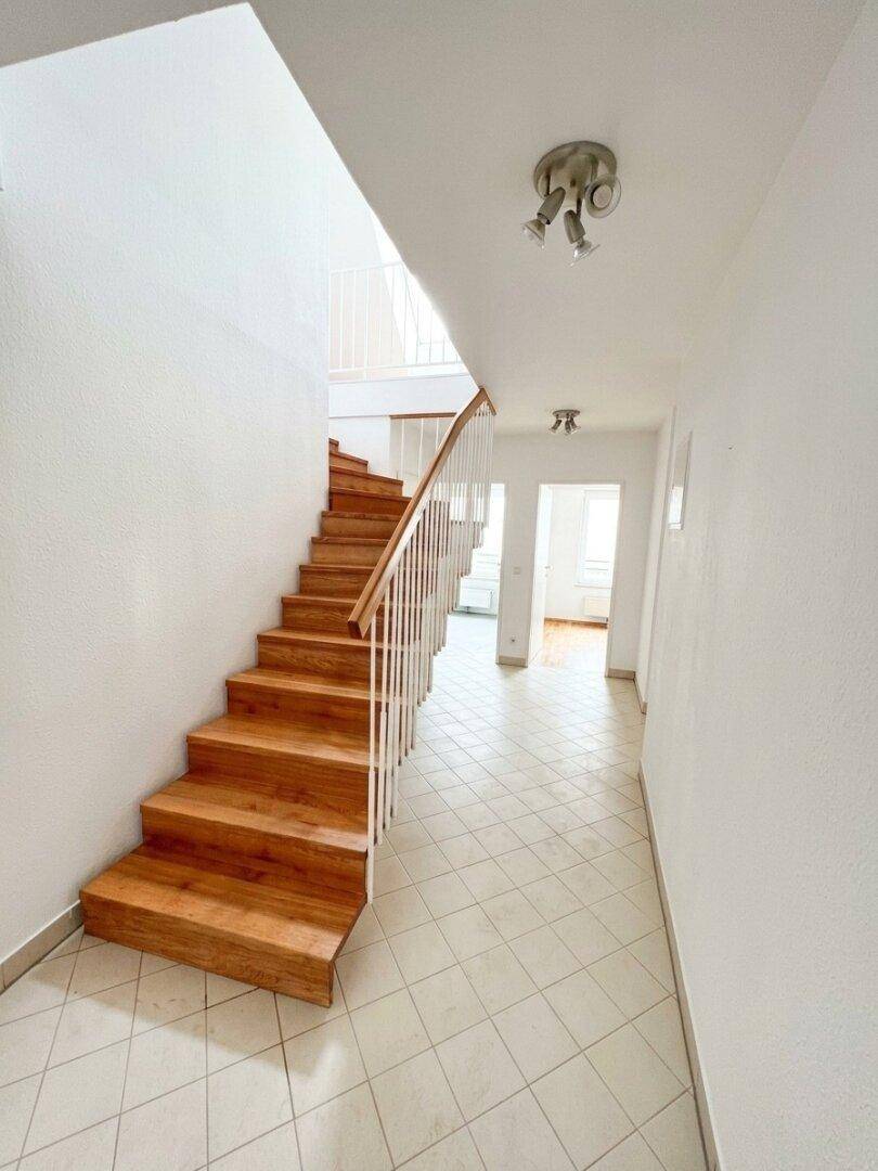 Heller Flur mit Holztreppe und Fliesenboden, der verschiedene Wohnbereiche verbindet.