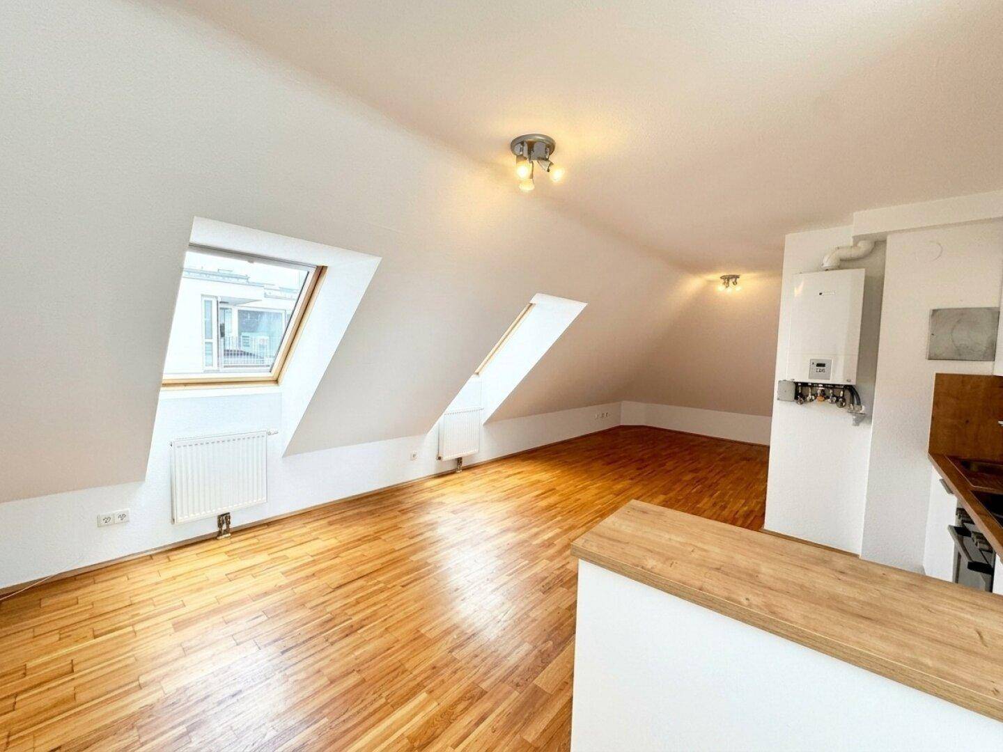 Helle Dachgeschosswohnung mit Holzboden, Dachschrägen und integrierter Küchenzeile.