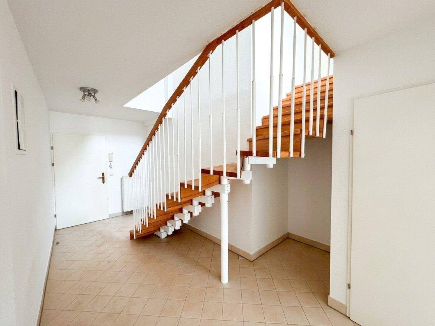 Geräumiger Flur mit Holztreppe und Fliesenboden, der zu den oberen Etagen führt.