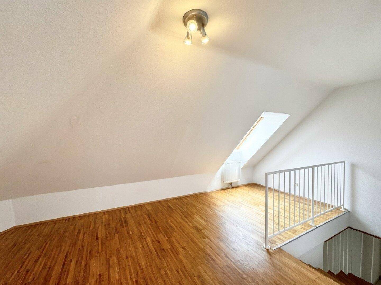 Geräumiger Dachgeschossraum mit Holzboden, Dachschrägen und einem großen Dachfenster.