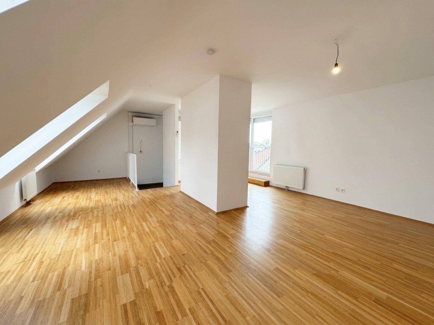 Geräumiger, unmöblierter Wohnbereich mit Holzboden, Dachschrägen und viel Tageslicht.