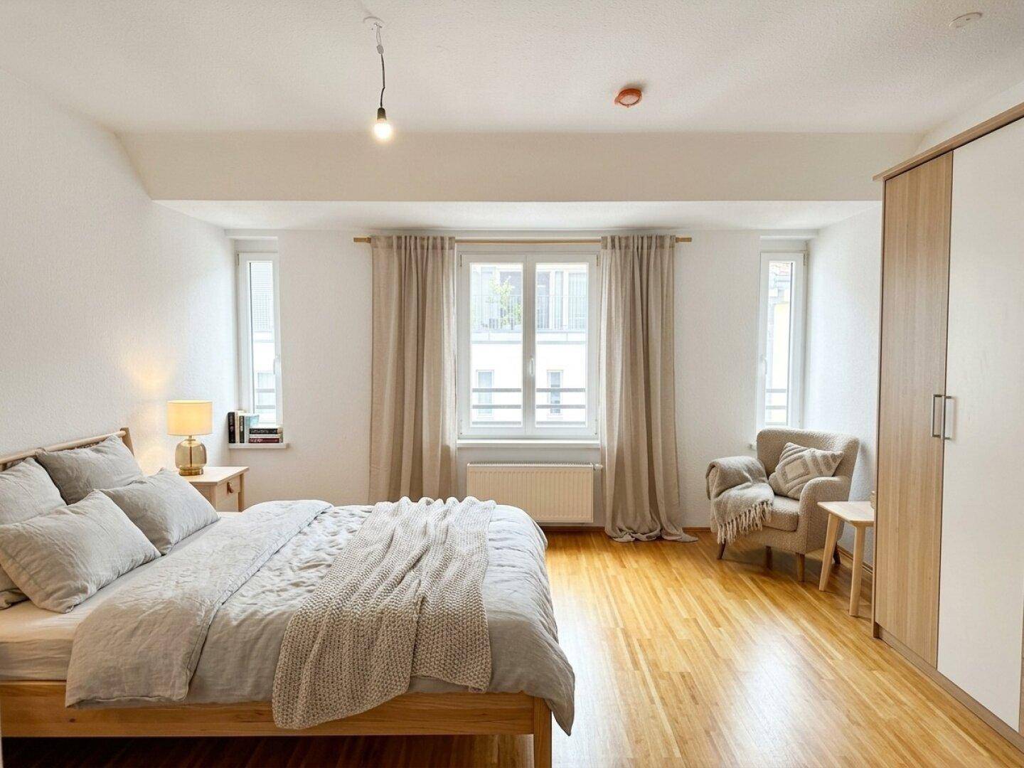 Gemütliches Schlafzimmer mit Holzboden, großem Bett und Vorhängen, hell und modern eingerichtet.