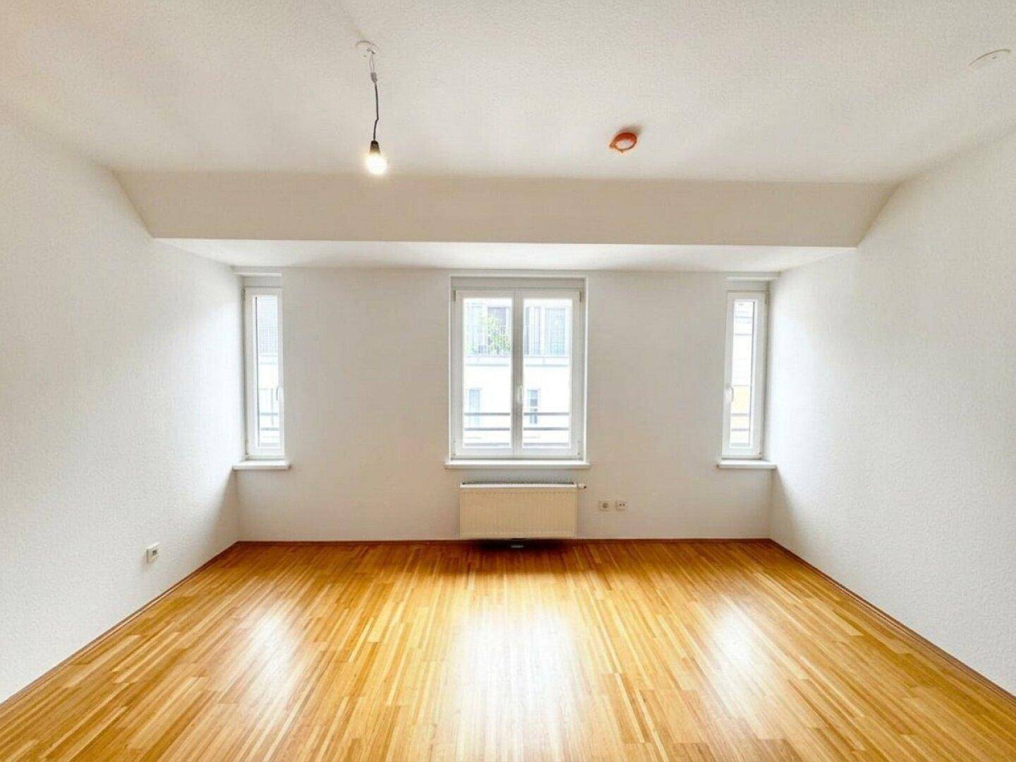 Heller, unmöblierter Raum mit Holzboden und großen Fenstern, ideal für Schlaf- oder Arbeitszimmer.