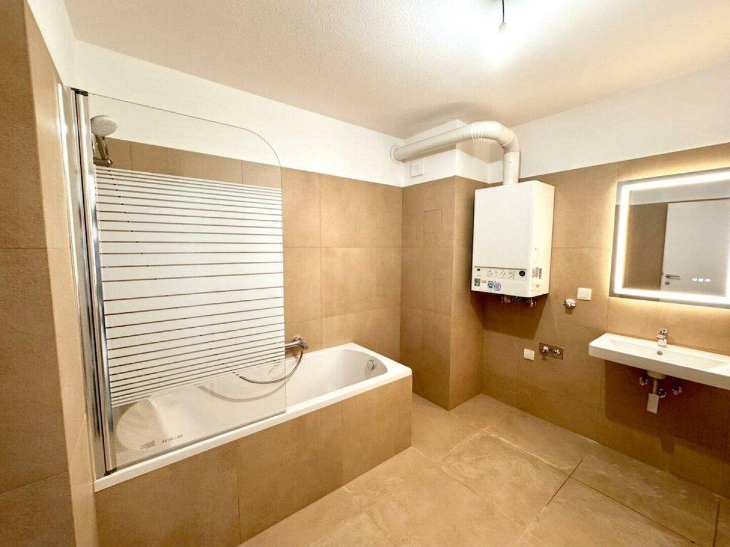 Modernes Badezimmer mit Badewanne, Dusche und beigefarbenen Fliesen, unmöbliert und funktional.