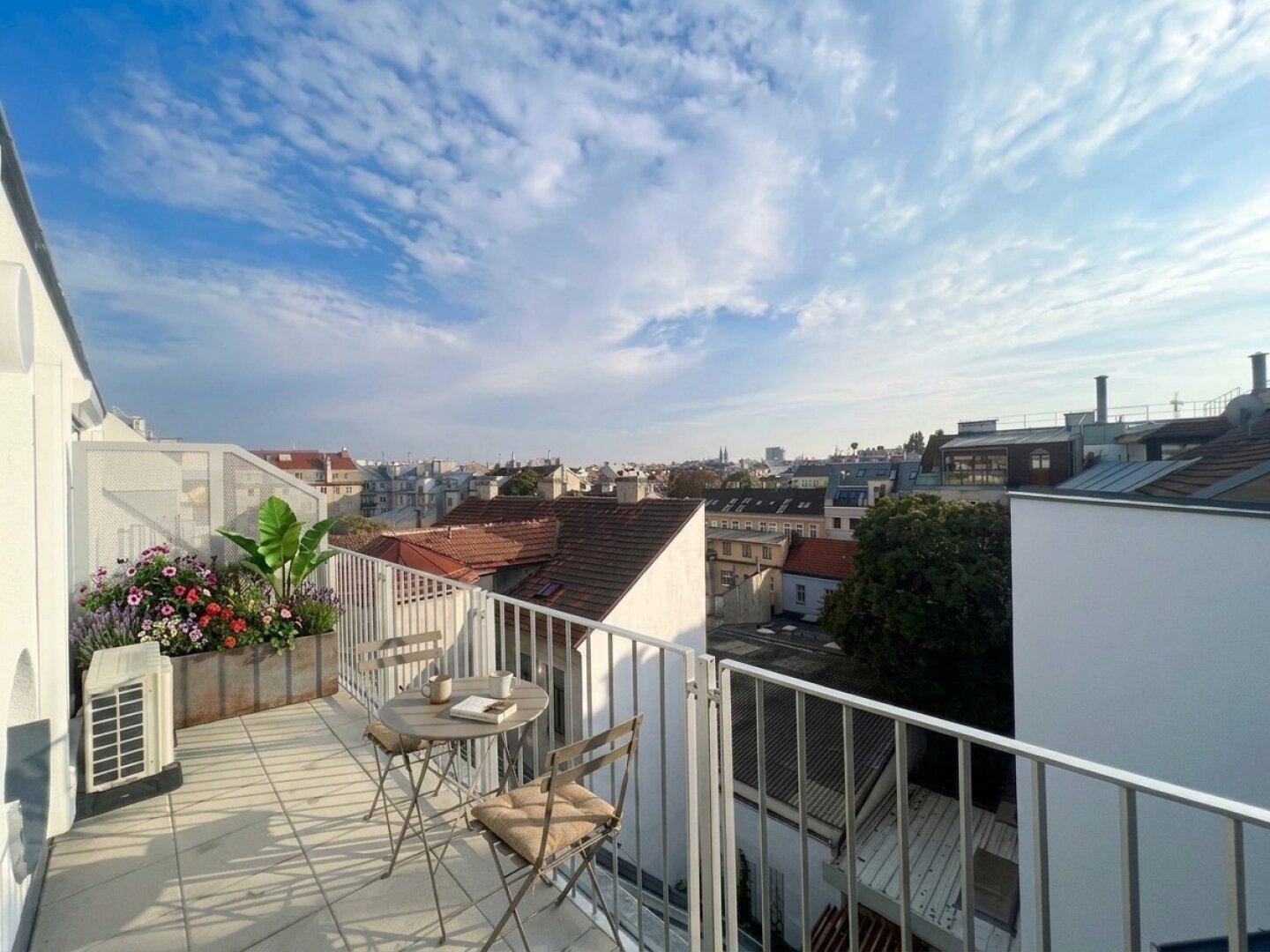 Möblierter Balkon mit Stadtblick, Sitzgelegenheiten und Pflanzen, ideal für sonnige Tage.