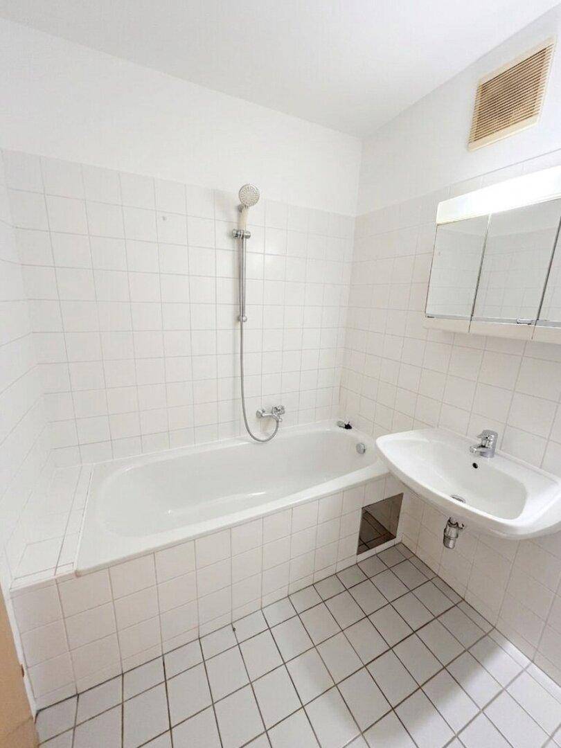 Funktionales Badezimmer mit Badewanne, Waschbecken und weißen Fliesen.