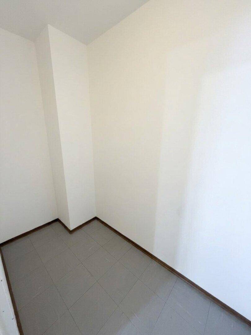 Kleiner, leerer Raum mit grauen Fliesen und weißen Wänden, vielseitig nutzbar.