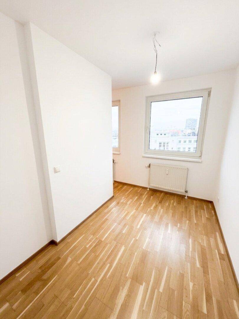 Helles Zimmer mit Parkettboden und großem Fenster, das einen Stadtblick bietet.
