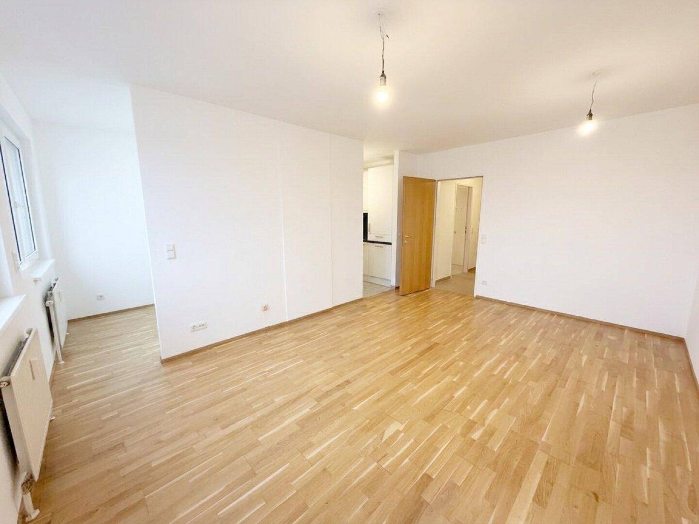 Geräumiges Zimmer mit hellem Parkettboden und Zugang zu weiteren Räumen.