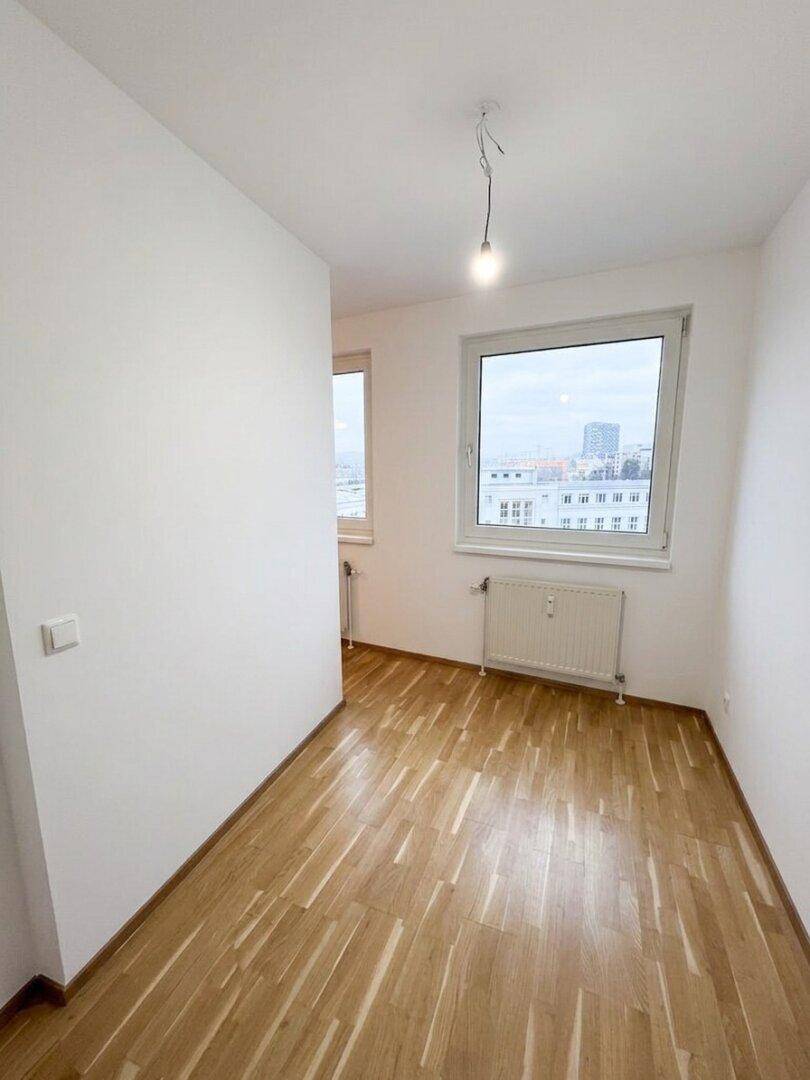 Helles Schlafzimmer mit Parkettboden, weiß gestrichenen Wänden und Stadtblick.