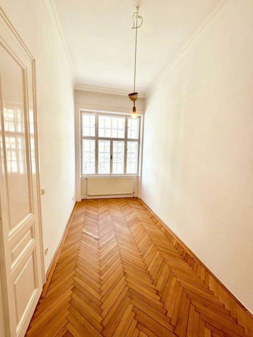 Heller Flur mit Fischgrätparkett und einem Fenster am Ende, das den Raum erhellt.