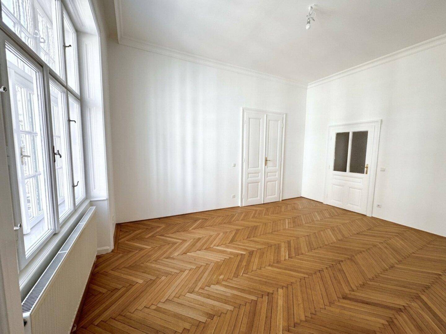 Heller Raum mit Fischgrätparkett und hohen Fenstern, die den Raum mit natürlichem Licht füllen.