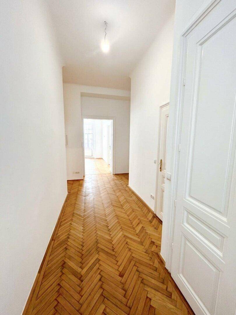 Langer Flur mit Fischgrätparkett und weißen Wänden, der einen Blick in weitere helle Räume bietet.