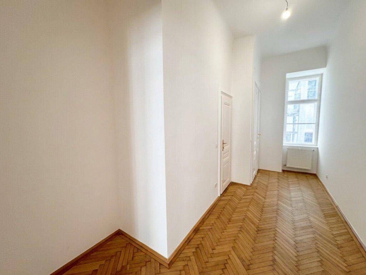 Heller Flur mit Fischgrätparkett und einem Fenster, das den Raum mit natürlichem Licht versorgt.