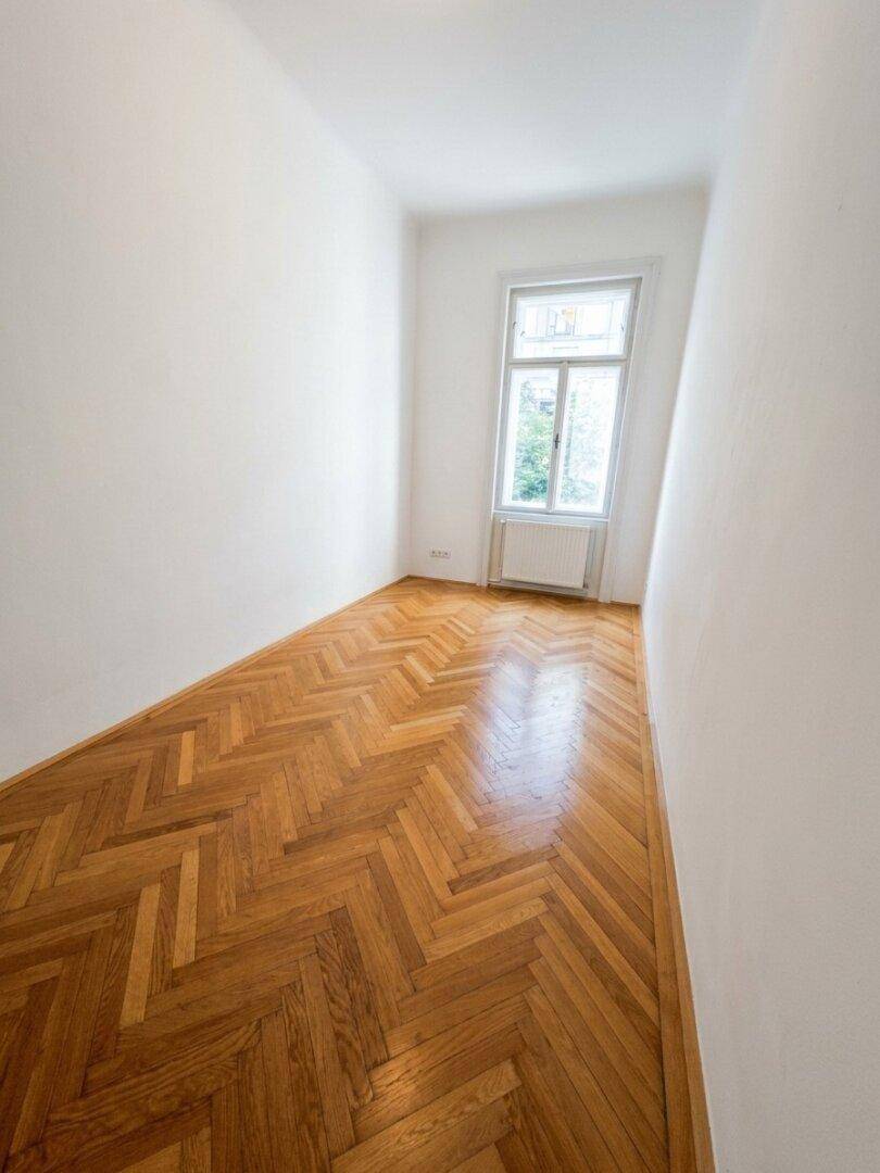 Kleines, helles Zimmer mit Fischgrätparkett und einem Fenster, ideal als Schlaf- oder Arbeitszimmer.