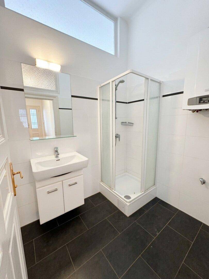 Modernes Badezimmer mit Duschkabine, Waschbecken und dunklen Bodenfliesen.