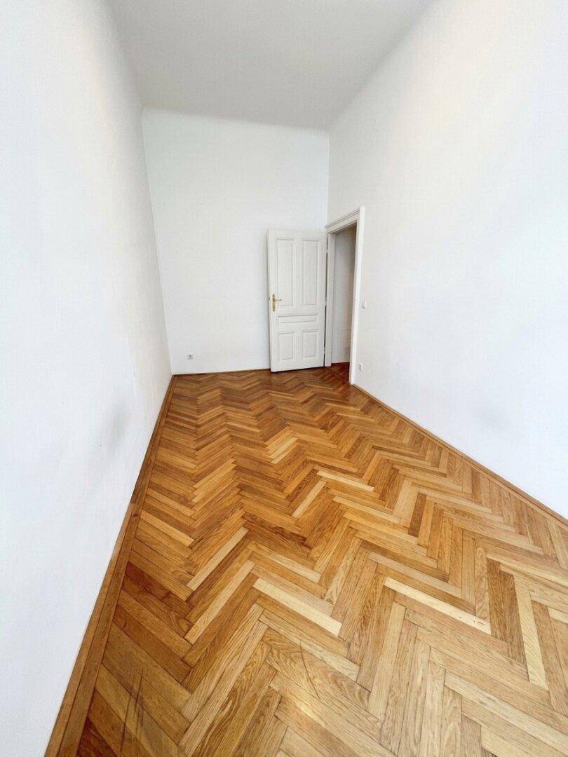 Leeres Zimmer mit Fischgrätparkett und einer Tür, bereit für neue Einrichtungsideen.