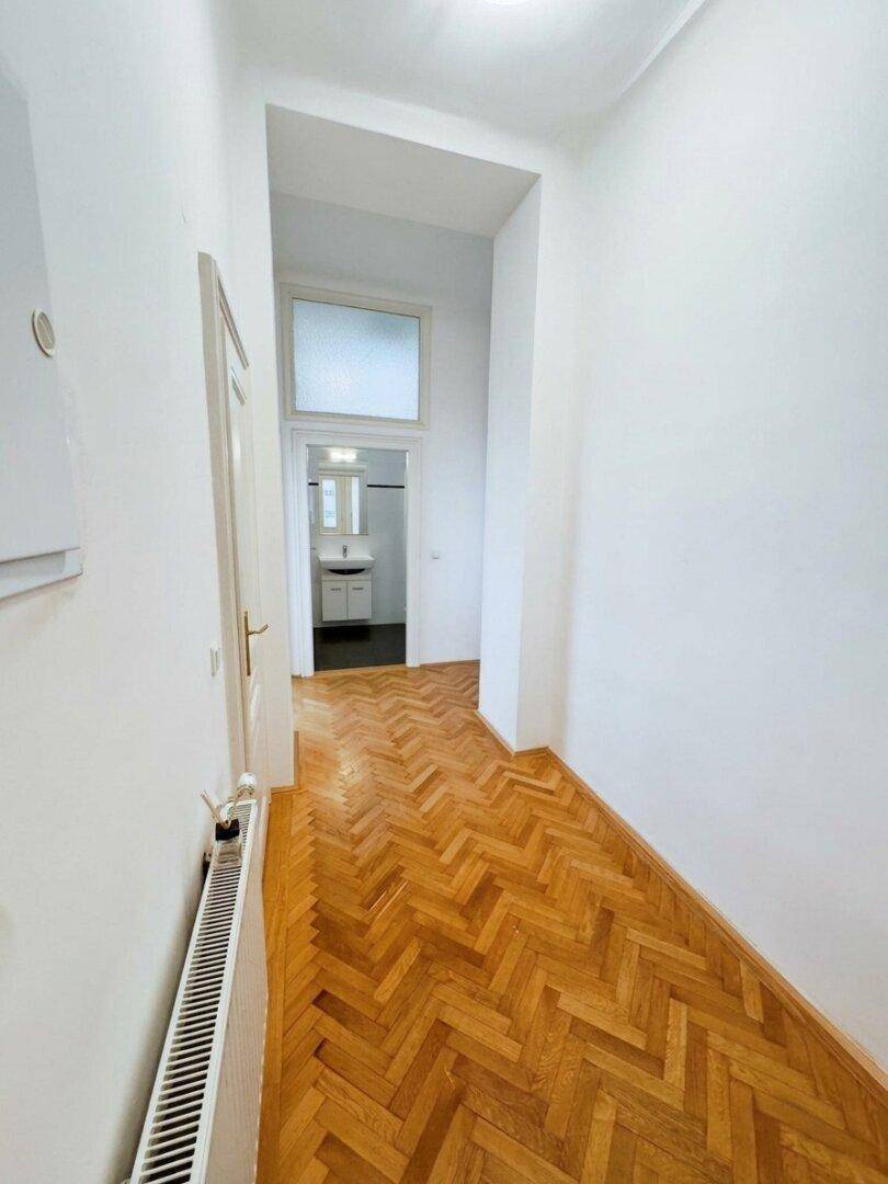 Heller Flur mit Fischgrätparkett, der zum Badezimmer führt, mit Blick auf das Waschbecken.