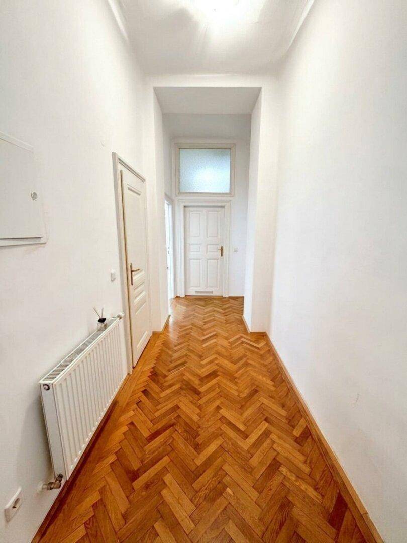 Geräumiger Flur mit Fischgrätparkett und hohen Decken, der zu weiteren Räumen führt.