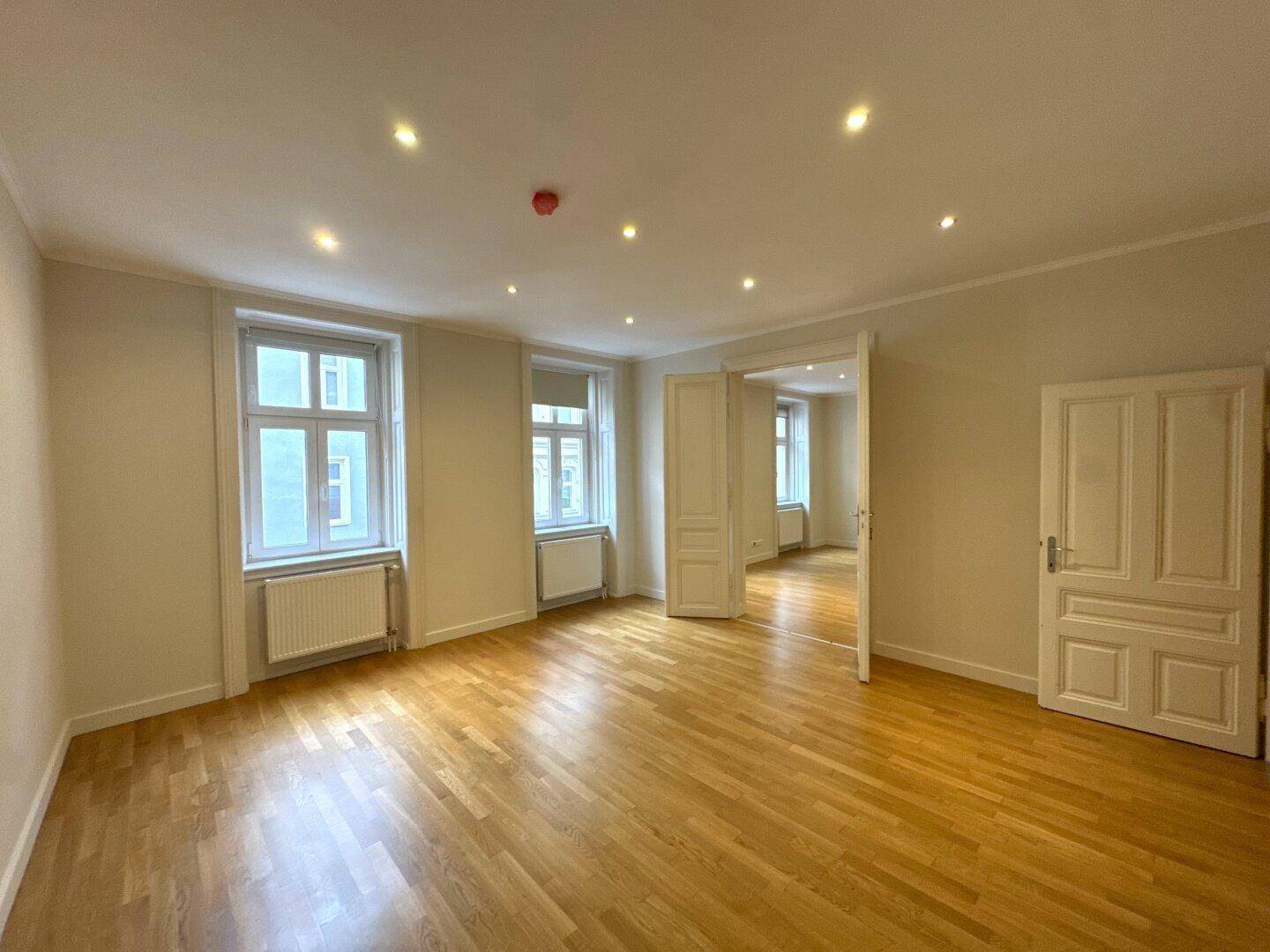 Geräumiges Zimmer mit hellem Parkettboden und mehreren Fenstern, ideal für Wohnzwecke.