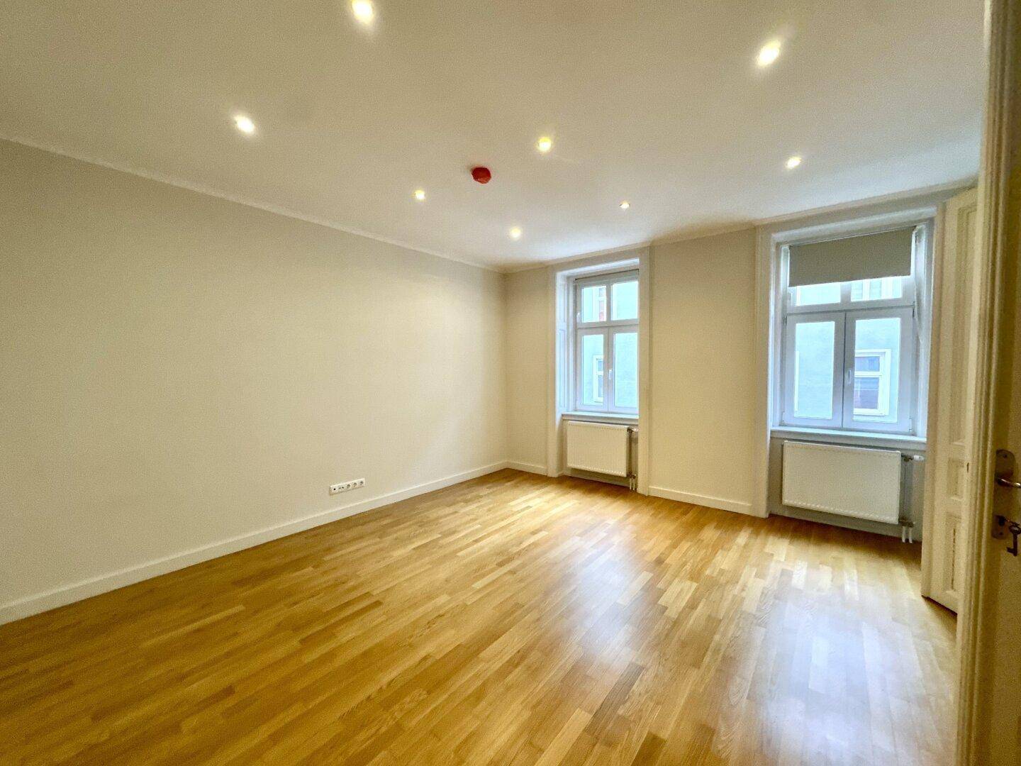 Leeres Zimmer mit hellem Parkettboden und zwei Fenstern, bereit zur individuellen Gestaltung.