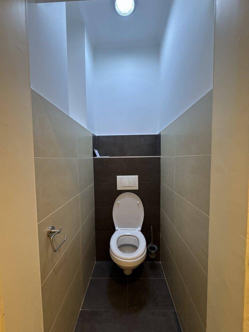 Kleines Gäste-WC mit Wand-WC und beigefarbenen Fliesen, minimalistisch gestaltet.