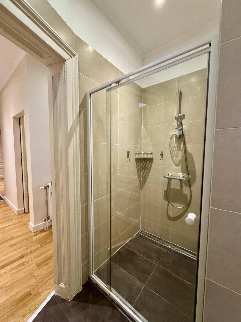 Duschbereich im Badezimmer mit Glasabtrennung und beigefarbenen Wandfliesen.
