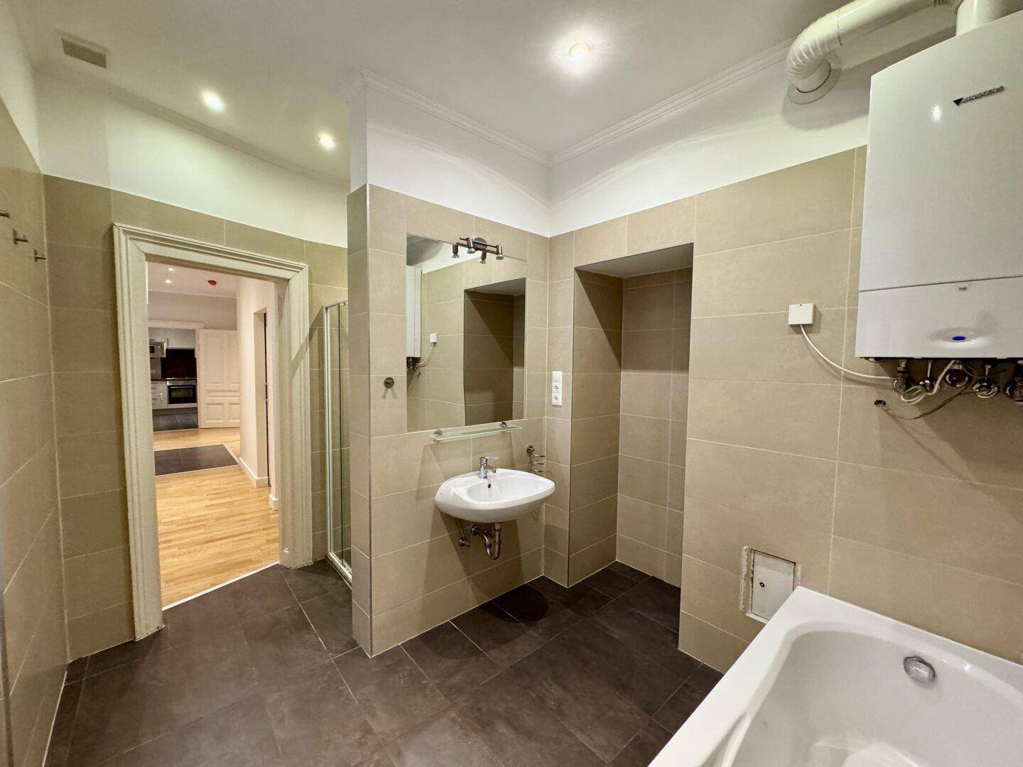 Geräumiges Badezimmer mit Badewanne, Waschbecken und Spiegel, mit Zugang zu anderen Räumen.