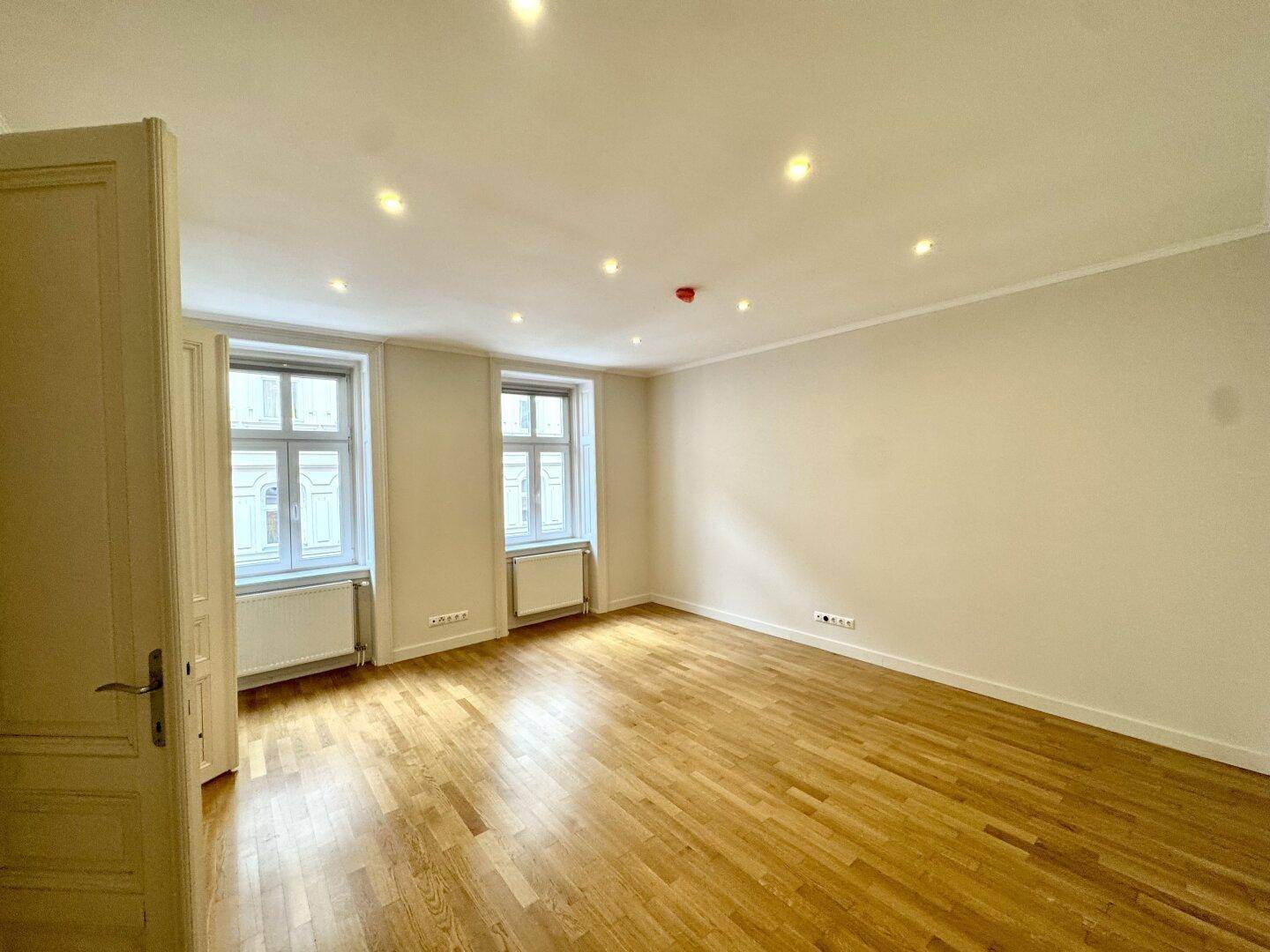 Helles Zimmer mit Parkettboden und zwei Fenstern, das eine angenehme Atmosphäre schafft.