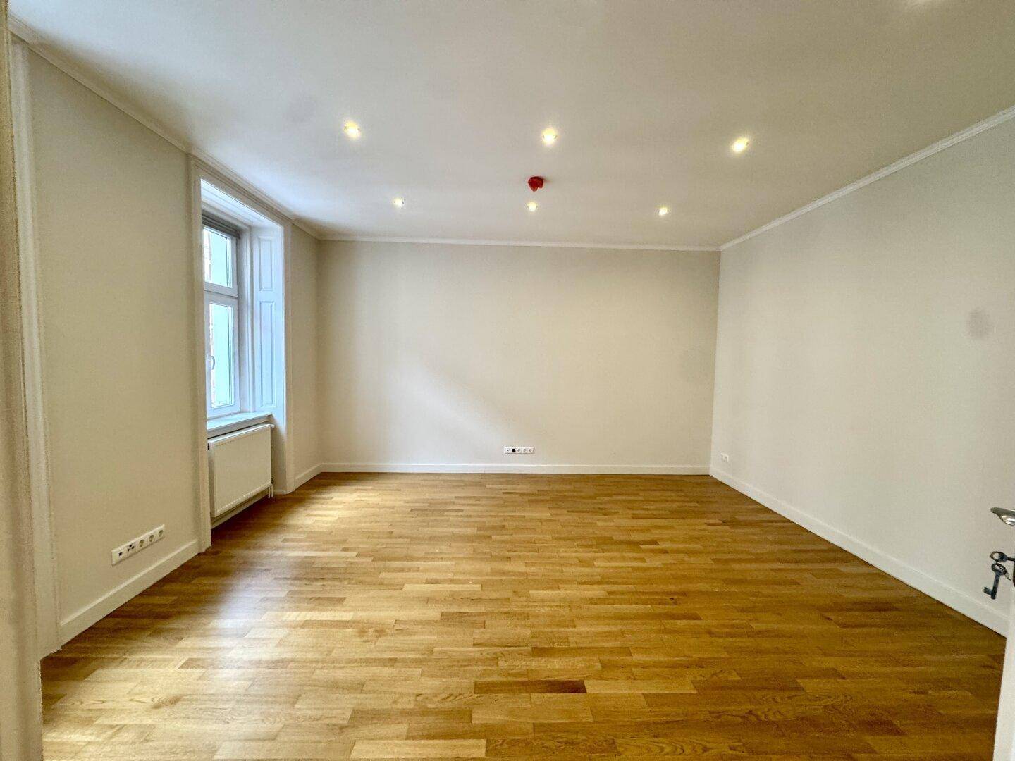 Leerer Raum mit Parkettboden und einem Fenster, das für ausreichend Belichtung sorgt.