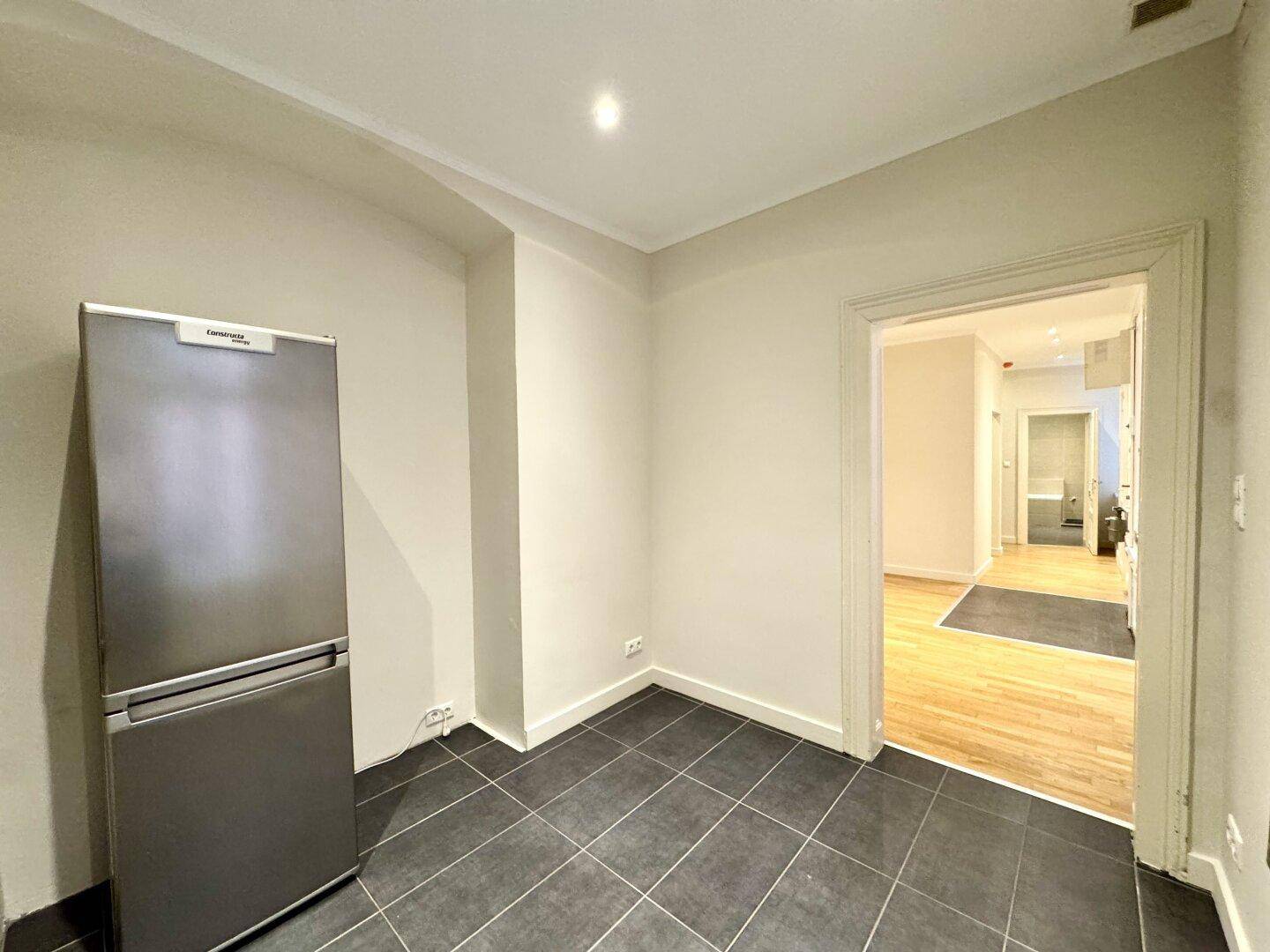 Küchenbereich mit Kühlschrank und gefliestem Boden, mit Blick in den Flur.