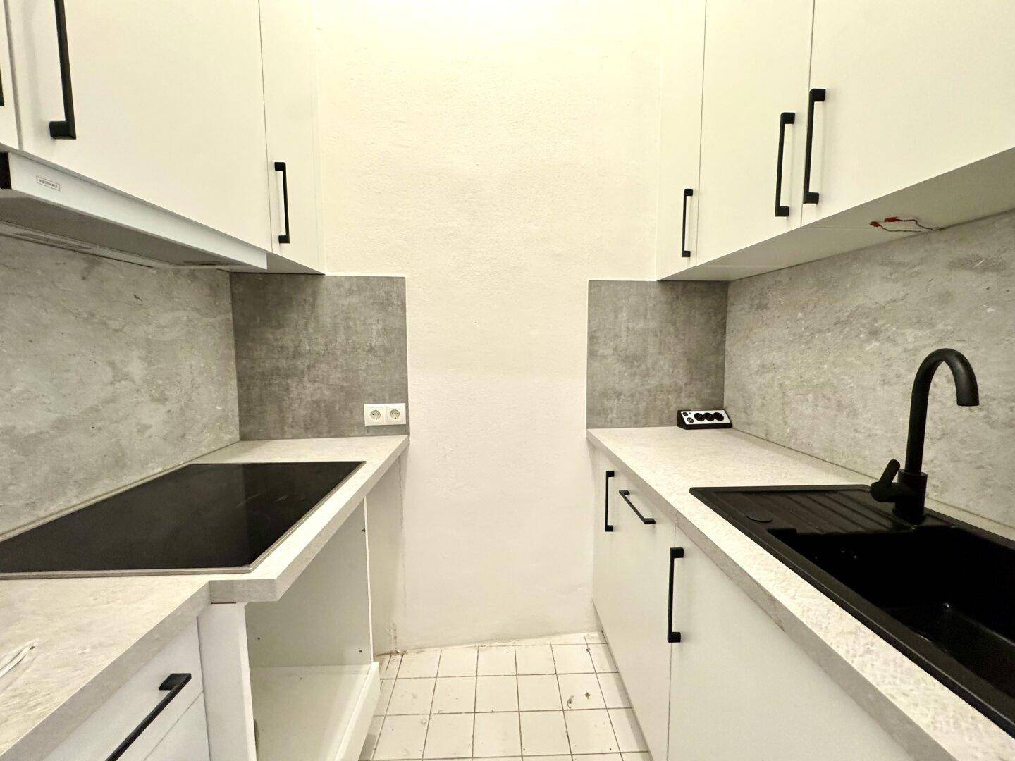 Neue, schmale Küche mit weißen Schränken, schwarzer Spüle und Induktionskochfeld.