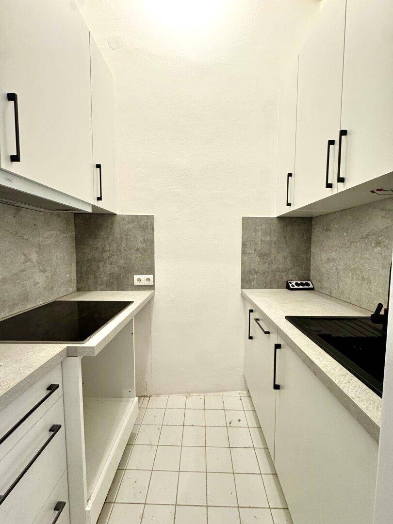 Moderne Küchenzeile mit weißen Fronten, schwarzem Wasserhahn und Fliesenboden.