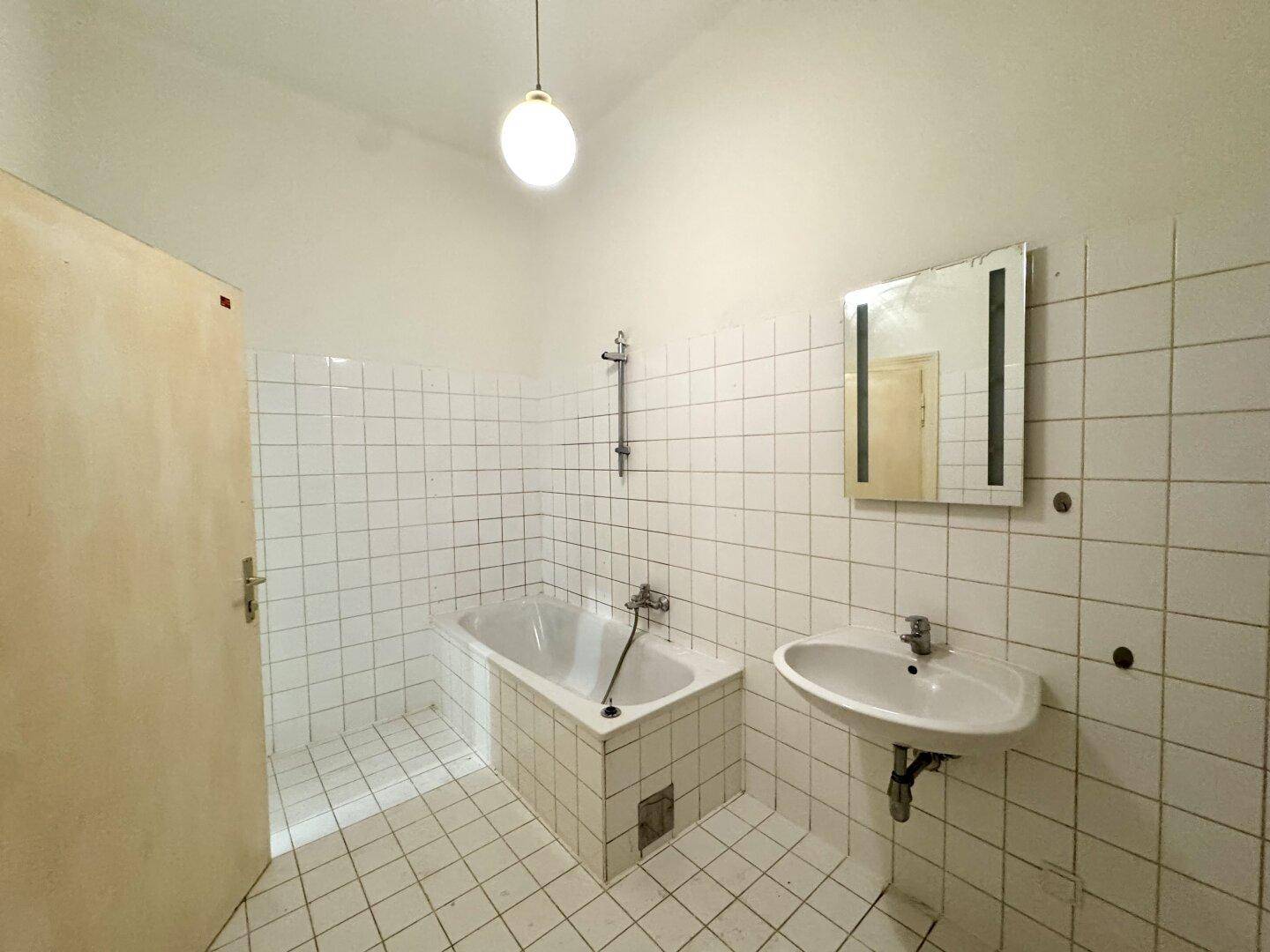 Einfaches Badezimmer mit weißen Fliesen, Badewanne und Waschbecken.