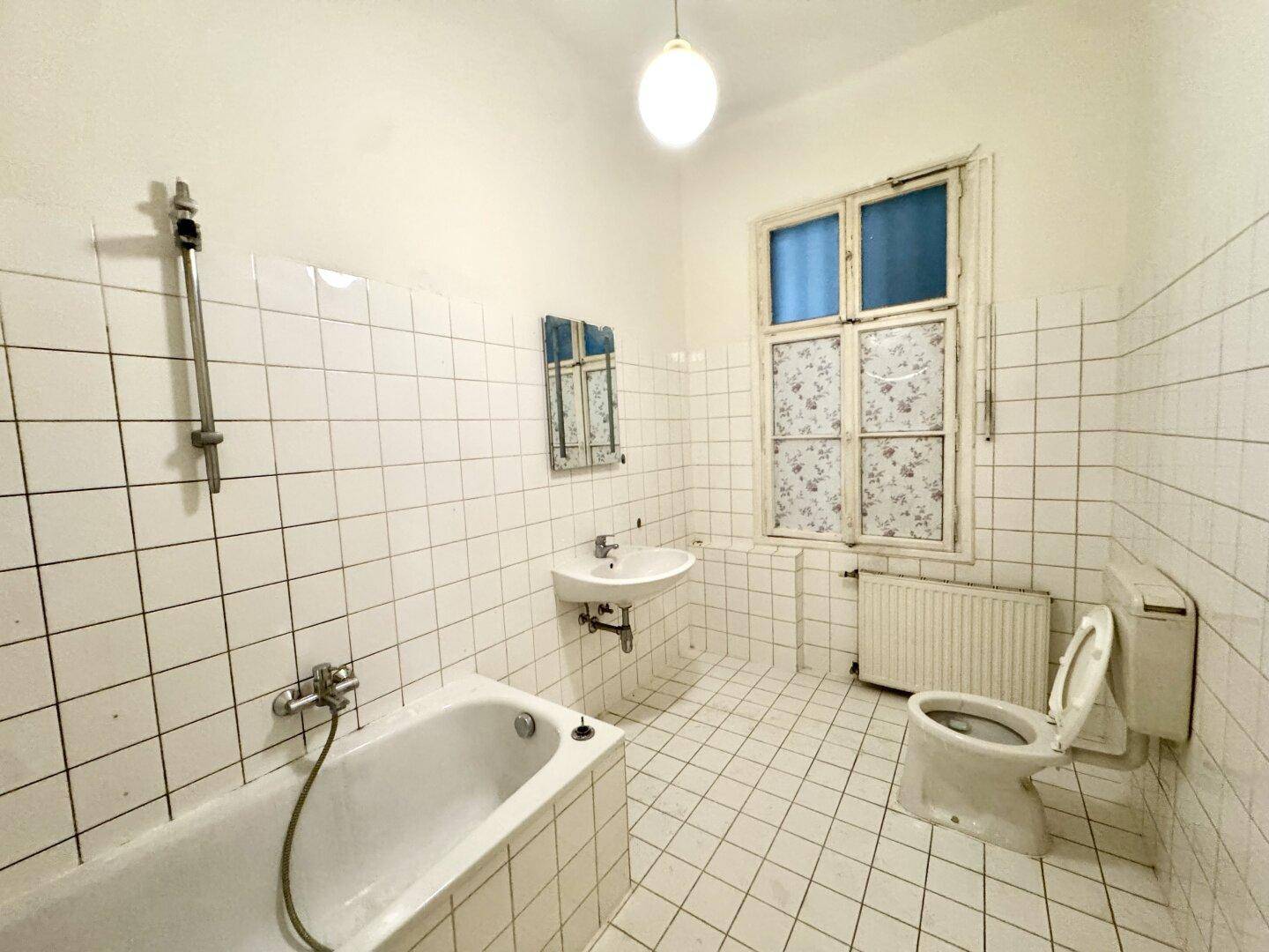 Gefliestes Badezimmer mit Badewanne, Waschbecken, Toilette und Fenster.