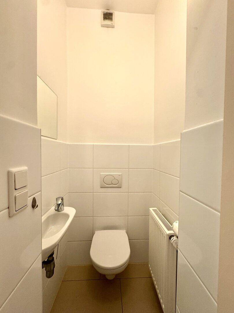 Kleines Gäste-WC mit Toilette, Handwaschbecken und Heizkörper, praktisch und sauber.