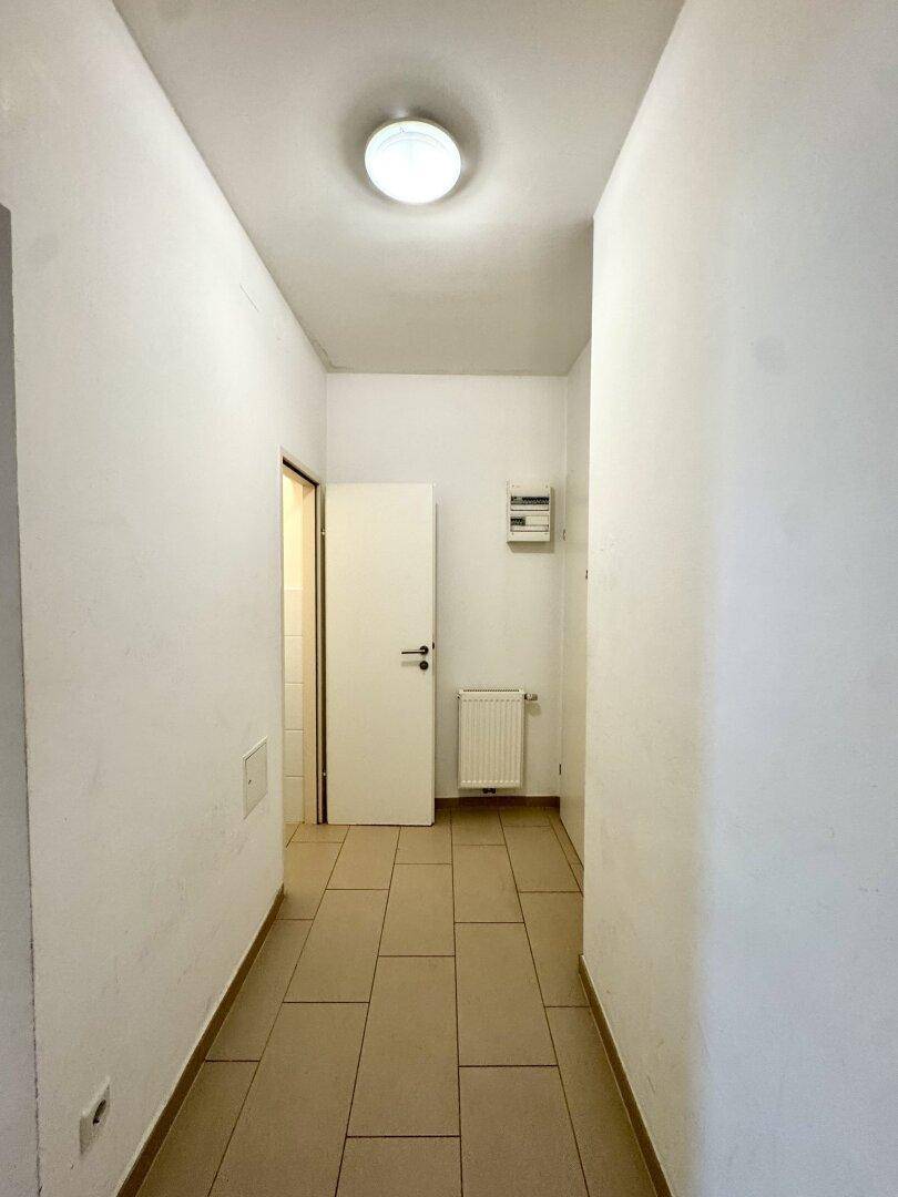 Heller Flur mit Fliesenboden und weiß gestrichenen Wänden, führt zu den angrenzenden Räumen.