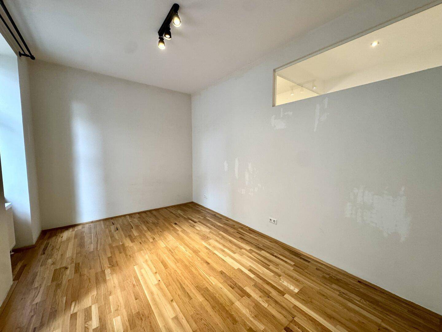 Zimmer mit Parkettboden und einer oberen Fensteröffnung, die für zusätzliche Helligkeit sorgt.