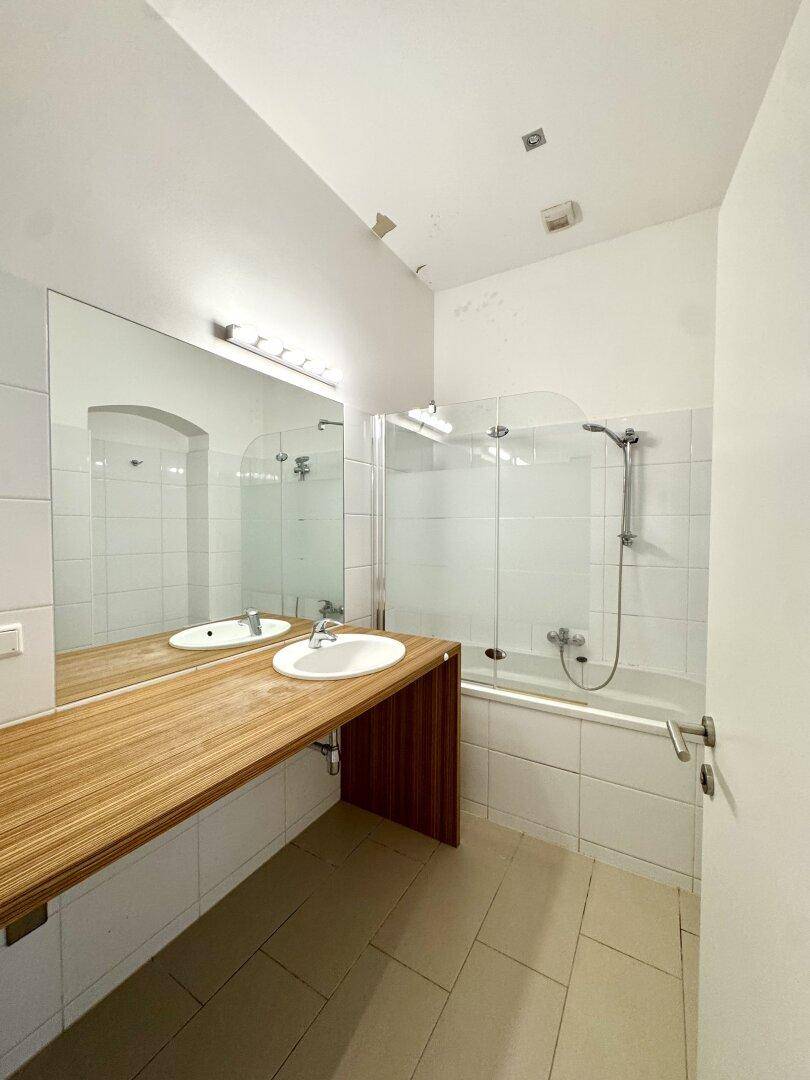 Modernes Badezimmer mit Badewanne, Dusche, Einzelwaschbecken und großem Spiegel, hell gefliest.