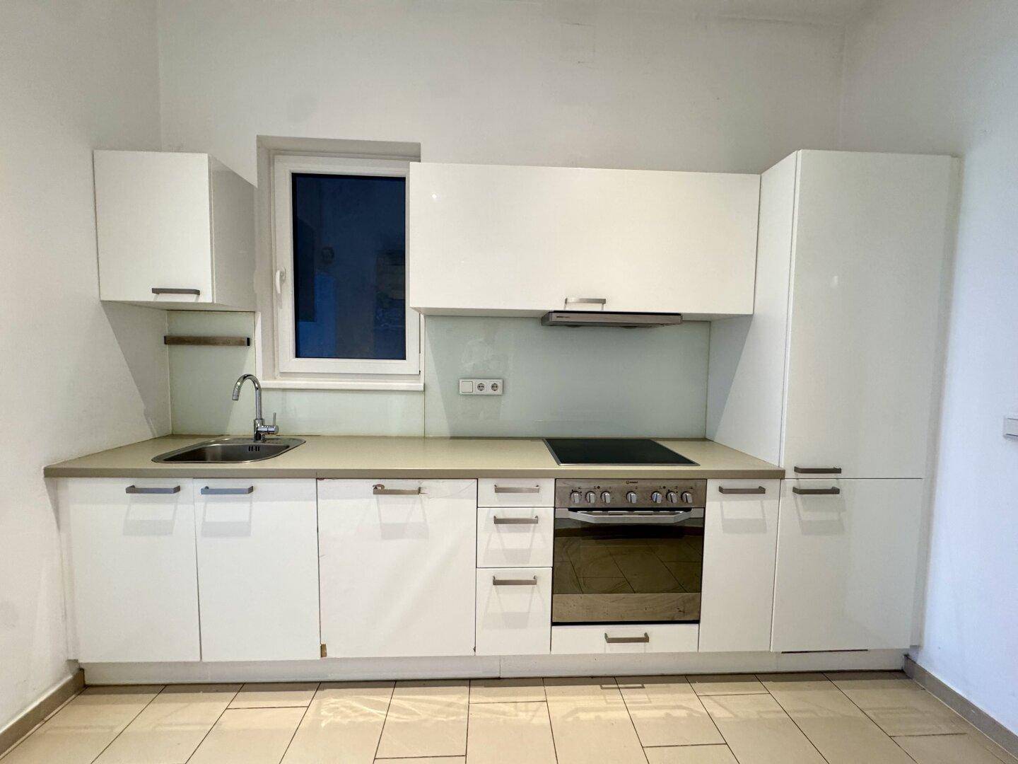 Moderne Küche mit weißen Schränken, Spüle, Induktionskochfeld und Backofen, funktional ausgestattet.