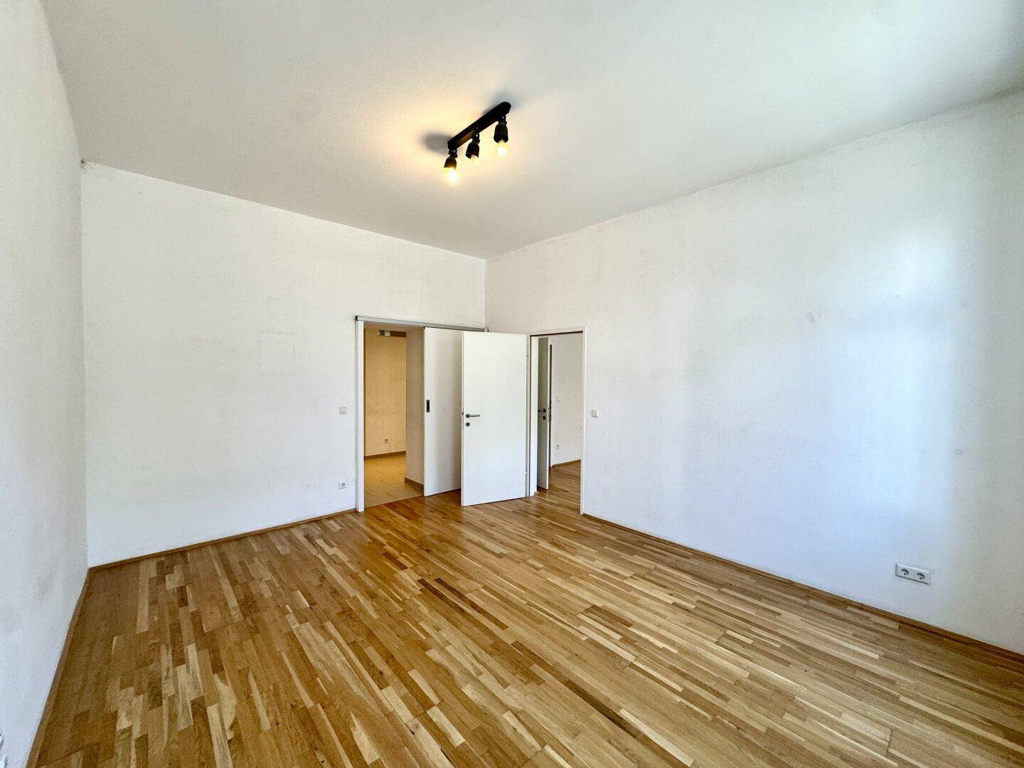 Geräumiges Zimmer mit Parkettboden und zwei offenen Türen, die den Zugang zu angrenzenden Bereichen ermöglichen.