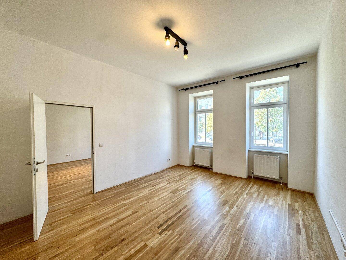Helles Zimmer mit Parkettboden, einem Fenster und offener Tür, bietet vielseitige Nutzungsmöglichkeiten.