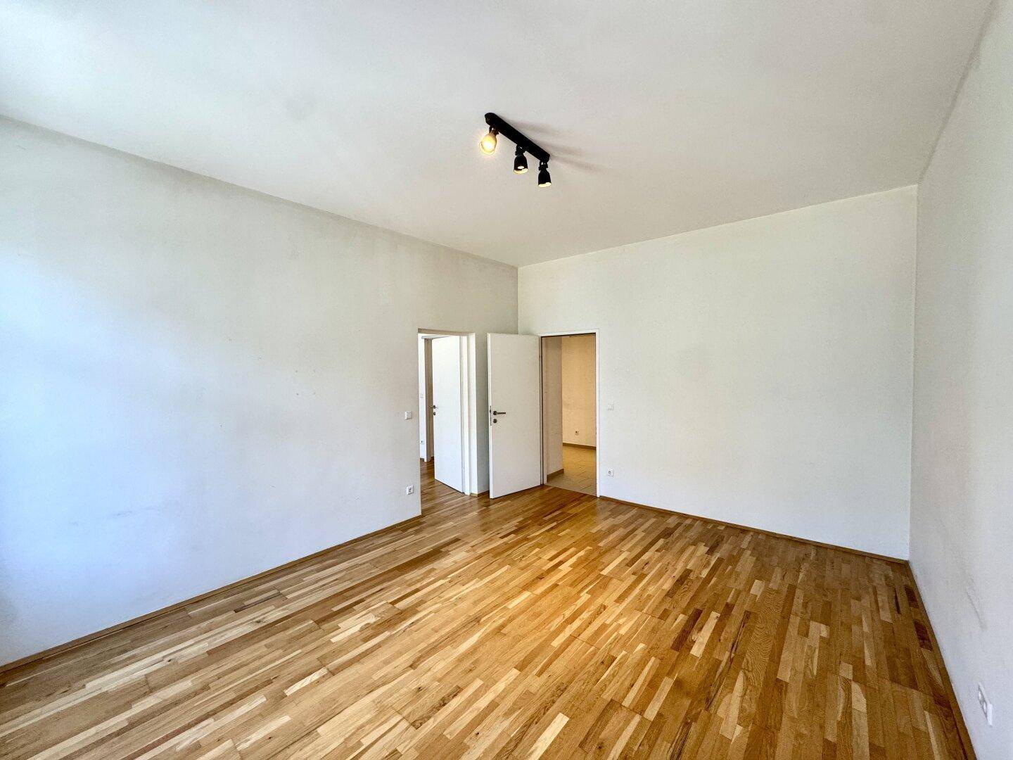 Geräumiges Zimmer mit Parkettboden und Zugang zu weiteren Räumen, hell und funktional gestaltet.