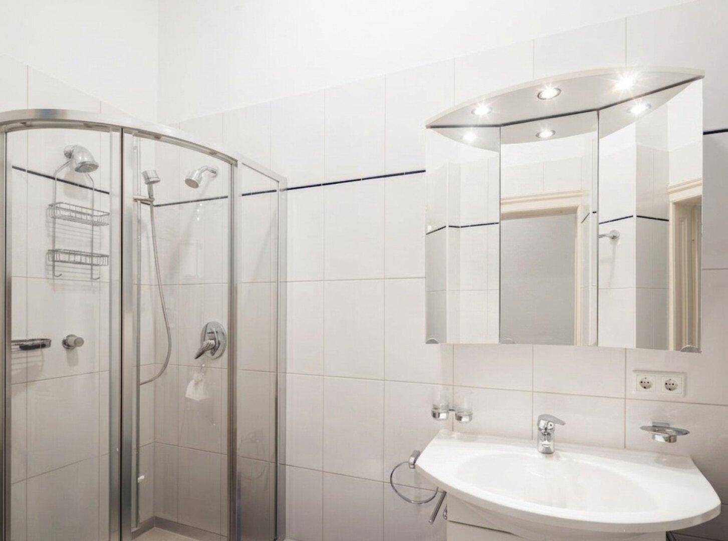 Gefliestes Badezimmer mit einer Duschkabine, Waschbecken und einem beleuchteten Spiegelschrank.